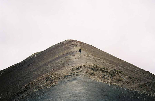 Solo hiker ascends rugged mountain peak under soft overcast sky, embodying adventure and solitude.