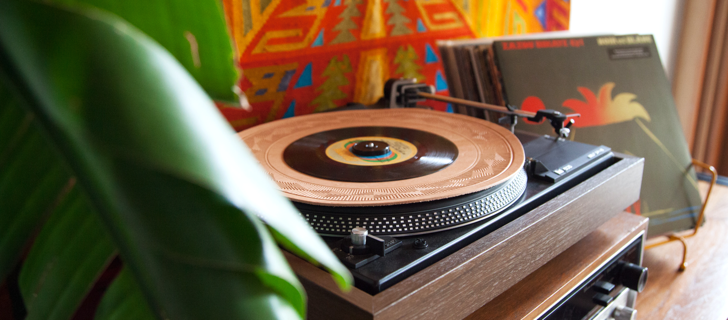 Vintage turntable with vinyl record, colorful geometric backdrop, lush green plant—cozy retro audio lifestyle.