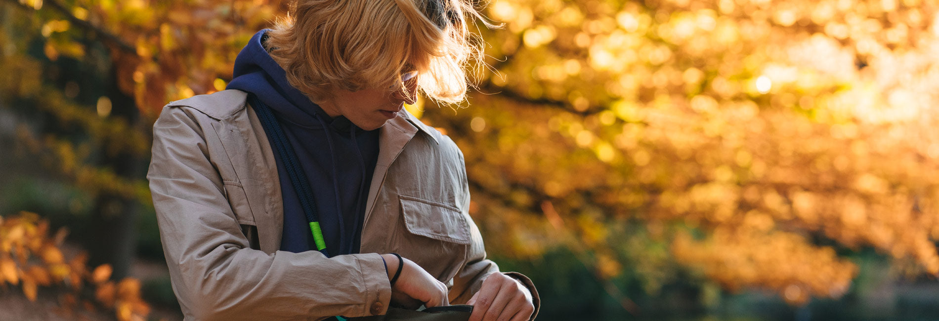 Golden autumn backdrop, woman in beige jacket and navy hoodie, stylish urban outdoor wear, warm earth tones, nature-inspired lifestyle.