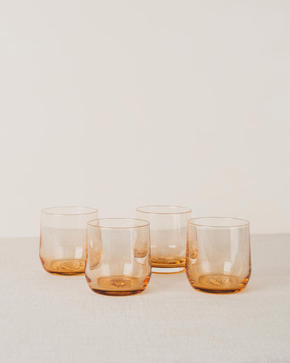 Four amber-tinted stemless cocktail glasses with an embossed pattern on the bottom, on a linen surface.