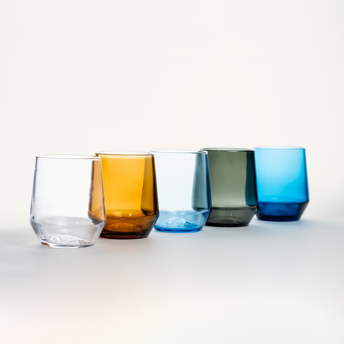 Set of five stemless wine glasses in clear, amber, blue, gray, and cobalt colors with faceted bases.