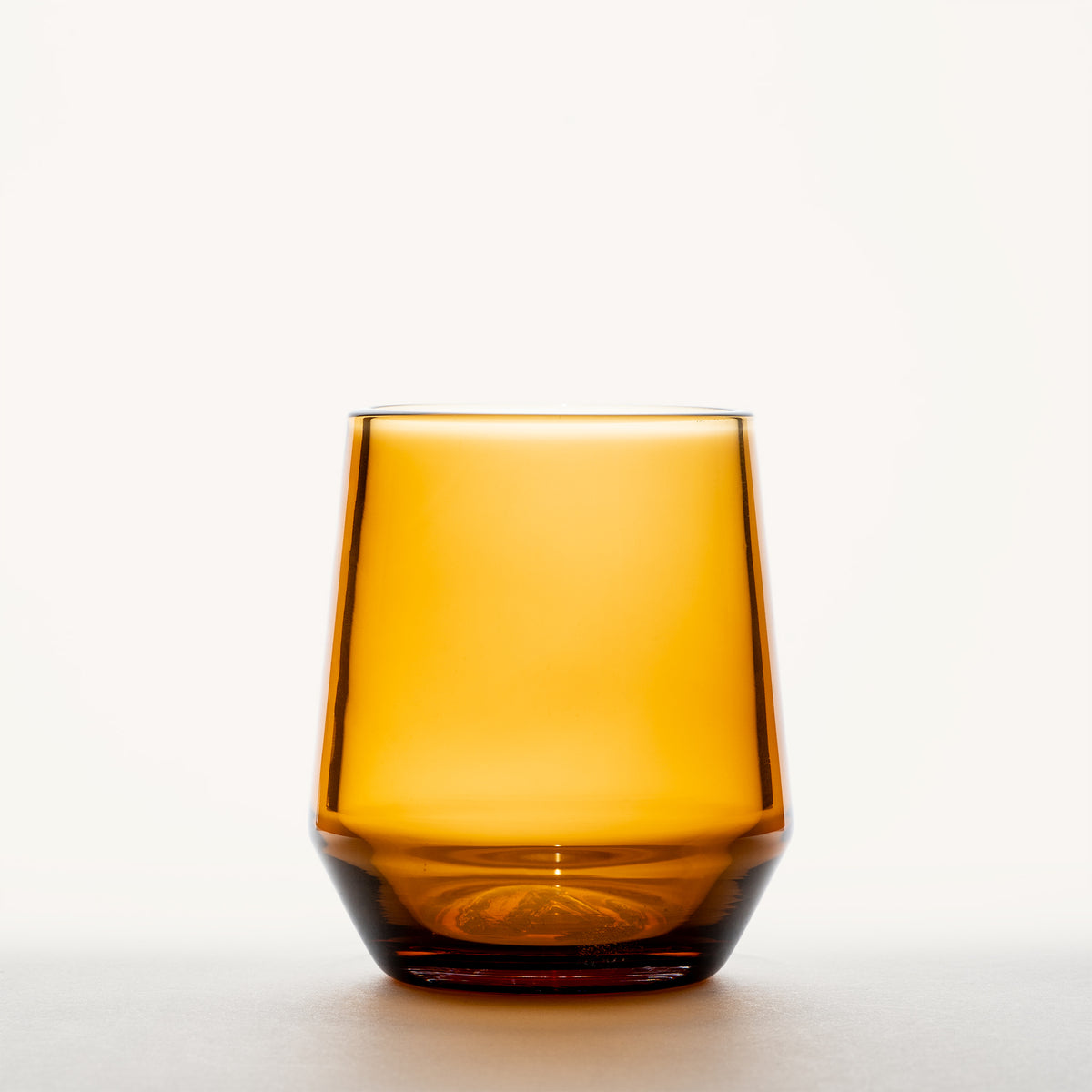 Amber wine glass with a thick, dark base and tapered stemless bowl, shown front-facing against a white background.