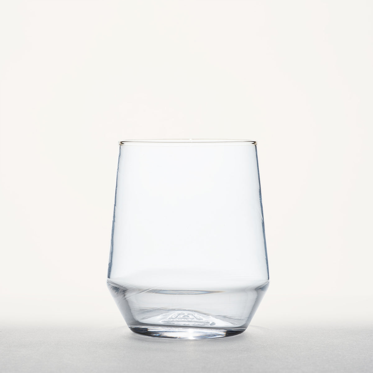 Clear stemless wine glass with a thick geometric base, photographed straight-on against a plain white background.