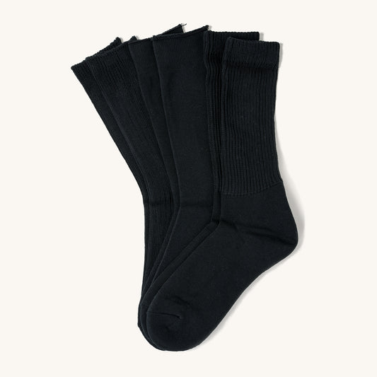 Three pairs of black crew socks with ribbed cuffs, layered side by side on a light background.