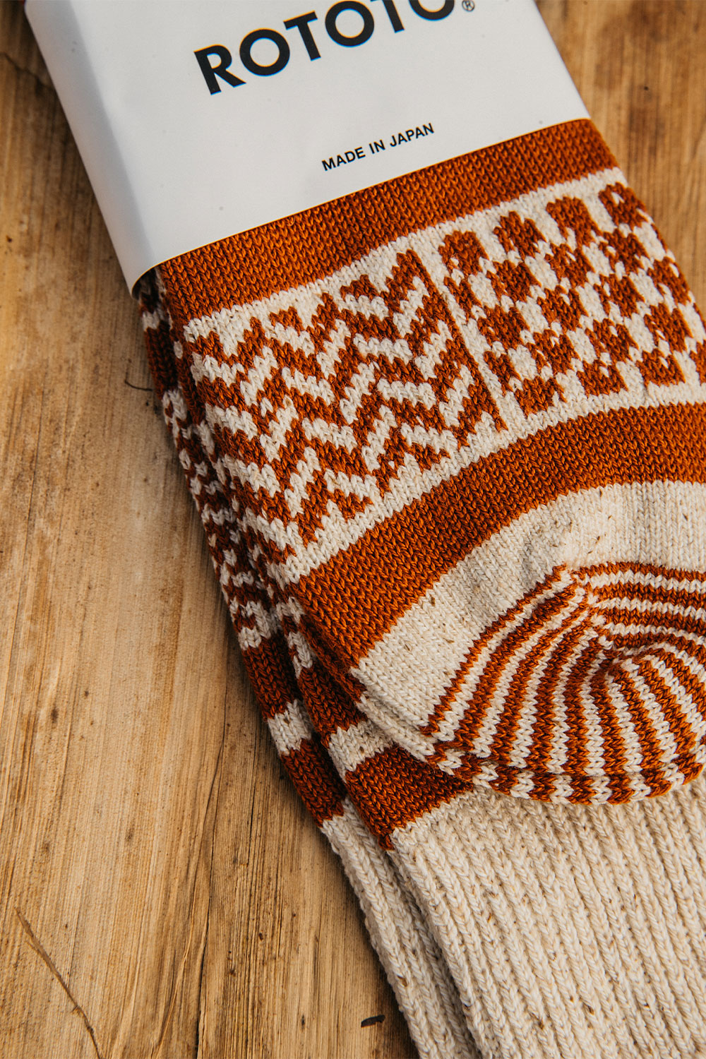 Ivory and rust multi jacquard crew socks with geometric patterns and ribbed details, lying on a wooden surface.