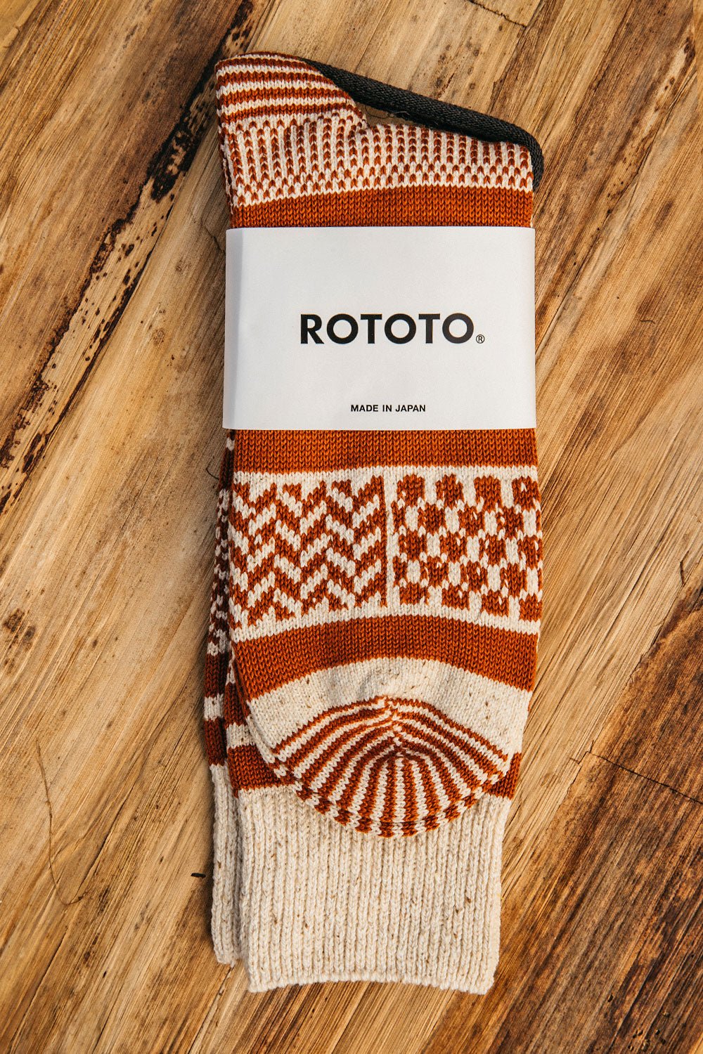 Ivory and rust multi jacquard crew socks from ROTOTO, featuring geometric patterns and a ribbed cuff, laid flat on wood.