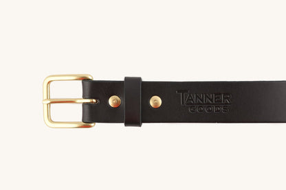 Black leather belt by Tanner Goods, featuring a brass buckle, gold-tone rivets, and an embossed logo.