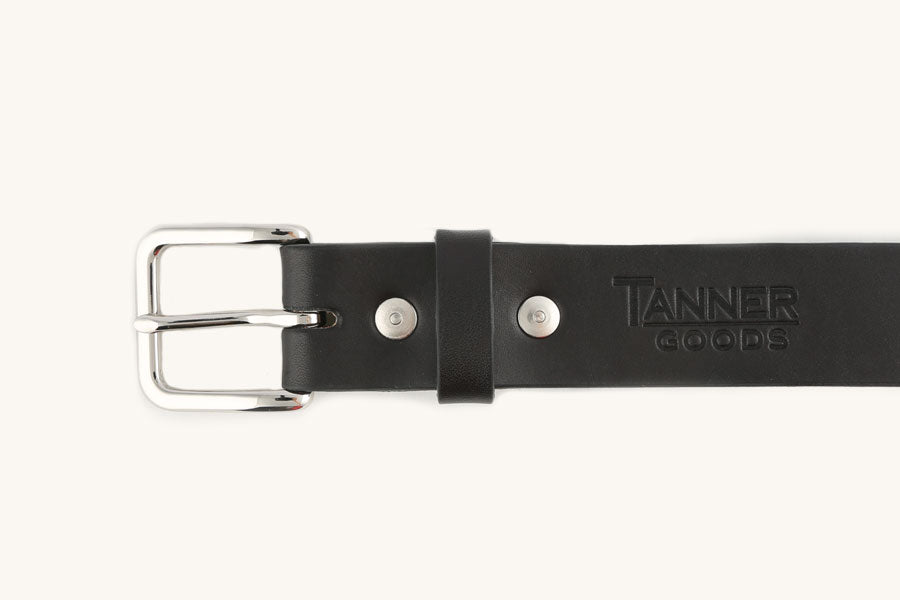Black leather belt by Tanner Goods with a polished silver buckle, two rivets, a keeper loop, and an embossed logo.