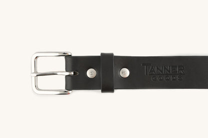 Black leather belt by Tanner Goods with a polished silver buckle, two rivets, a keeper loop, and an embossed logo.