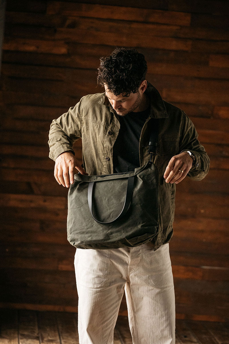 Juniper Green waxed canvas Simple Tote, carried by a man wearing an olive jacket and reaching inside.