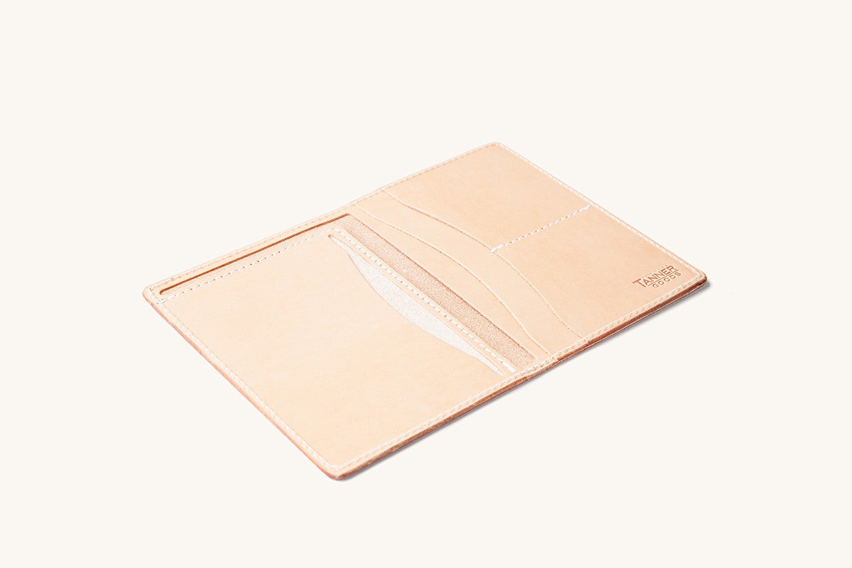 Natural leather travel wallet by Tanner Goods, open to show multiple card slots and an embossed logo.